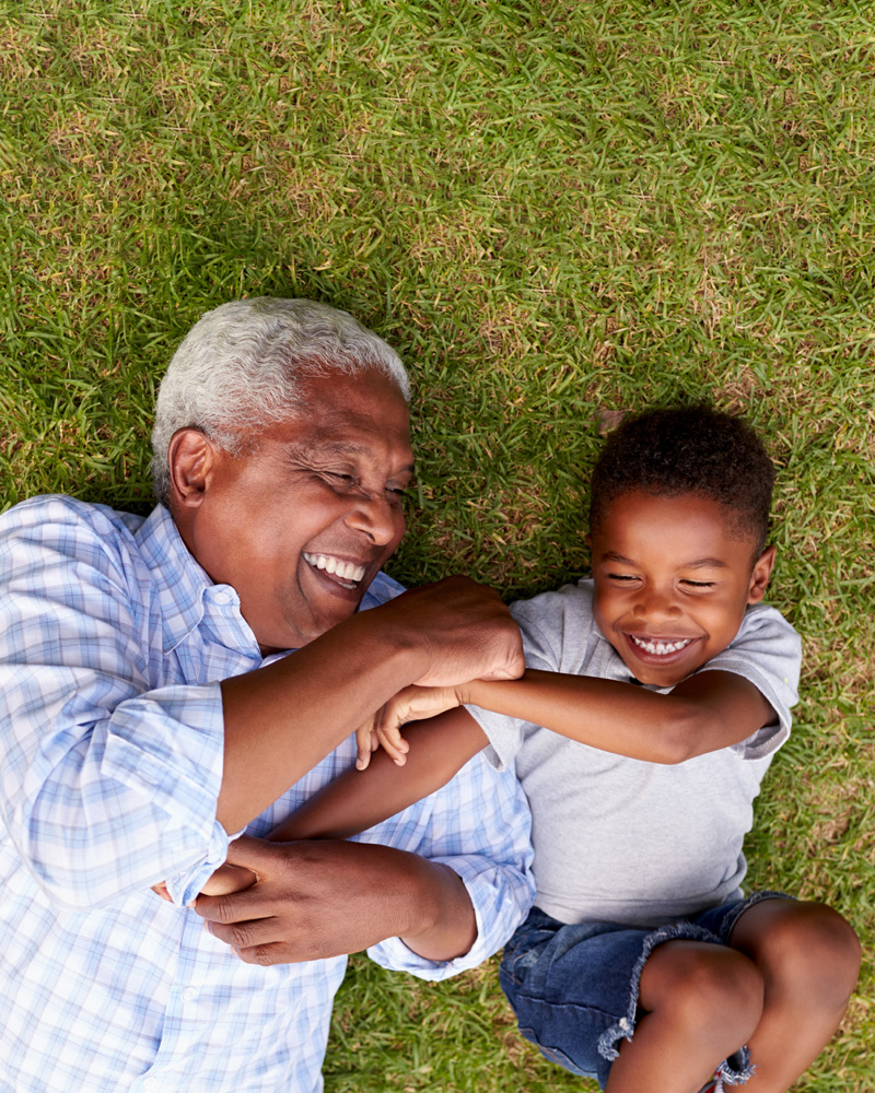 An older man and young boy laying on the grass smiling