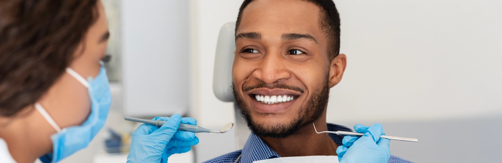 A smiling man with white teeth is sitting in a dental chair while looking at a female dentist