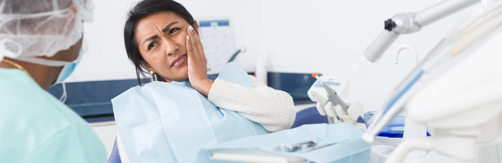 A woman with a cavity sitting in a dental chair, holding her jaw with a pained expression