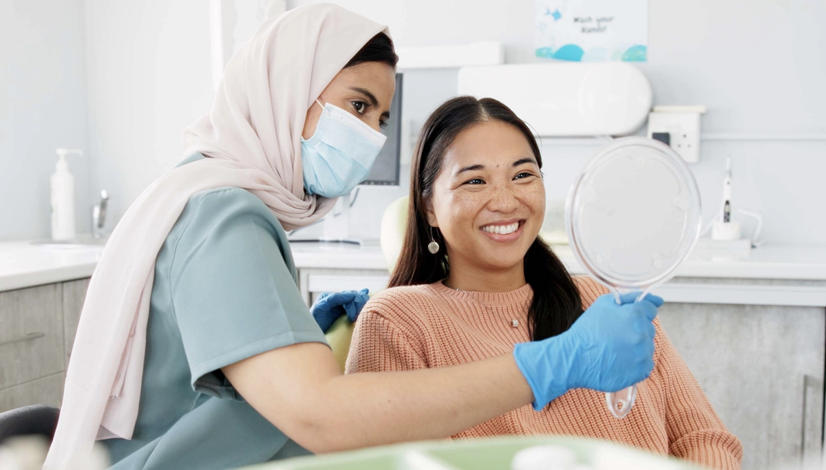 A dentist holding up a mirror for her smiling patient who is smiling and looking at her new dental crown