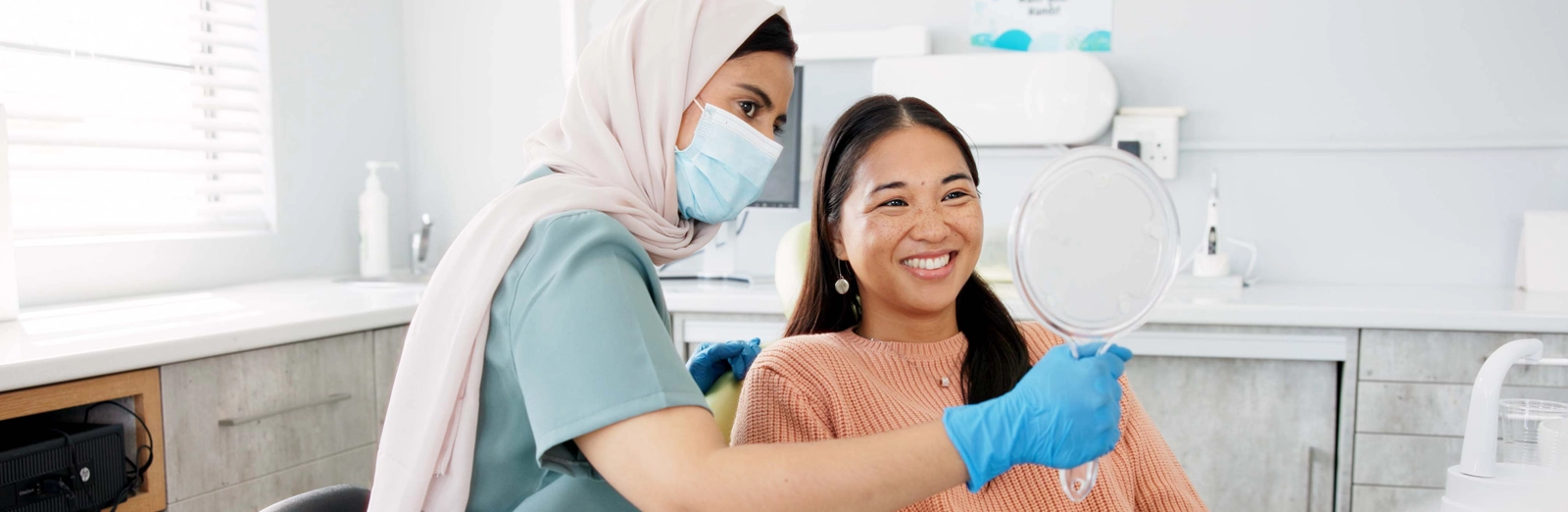 A dentist holding up a mirror for her smiling patient who is smiling and looking at her new dental crown