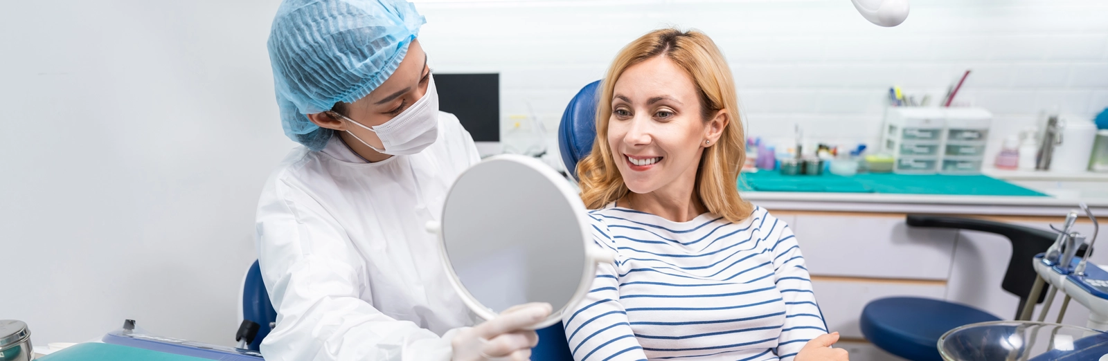 woman-looking-in-mirror-at-dental-office-1600x522.webp