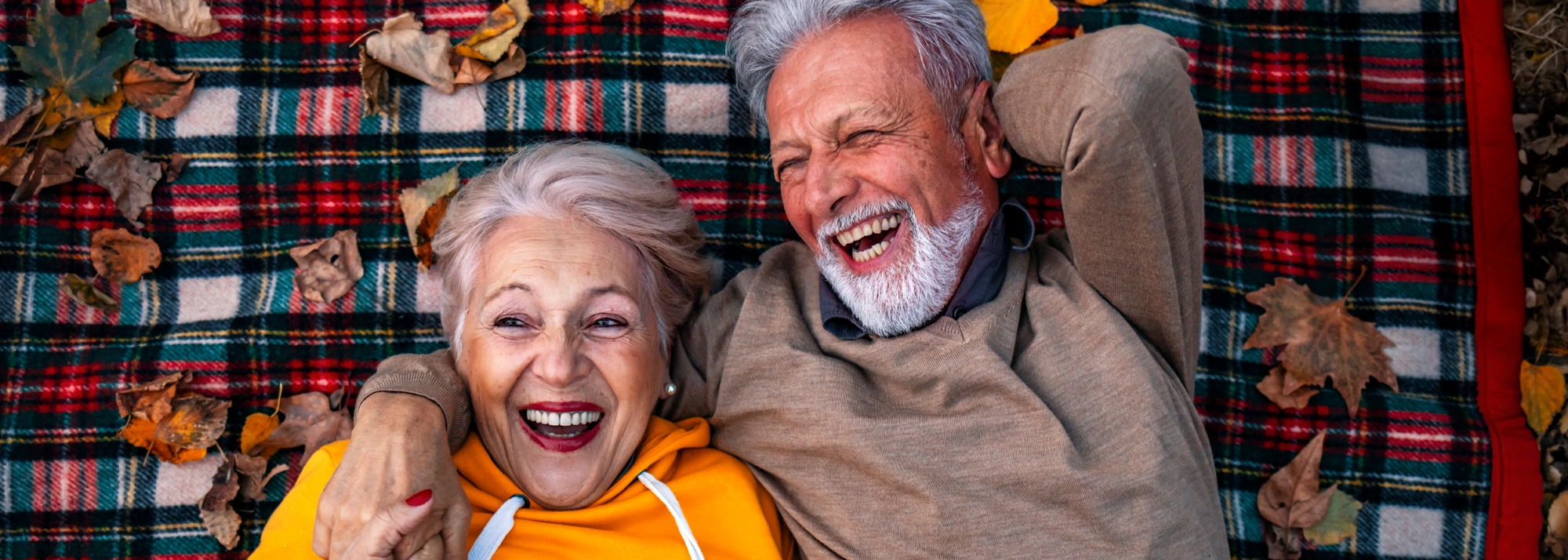 older_couple_laying_on_blanket_laughing_2000x714.webp