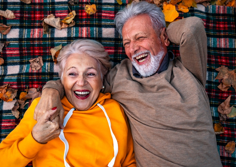 older_couple_laying_on_blanket_laughing_767x544.webp