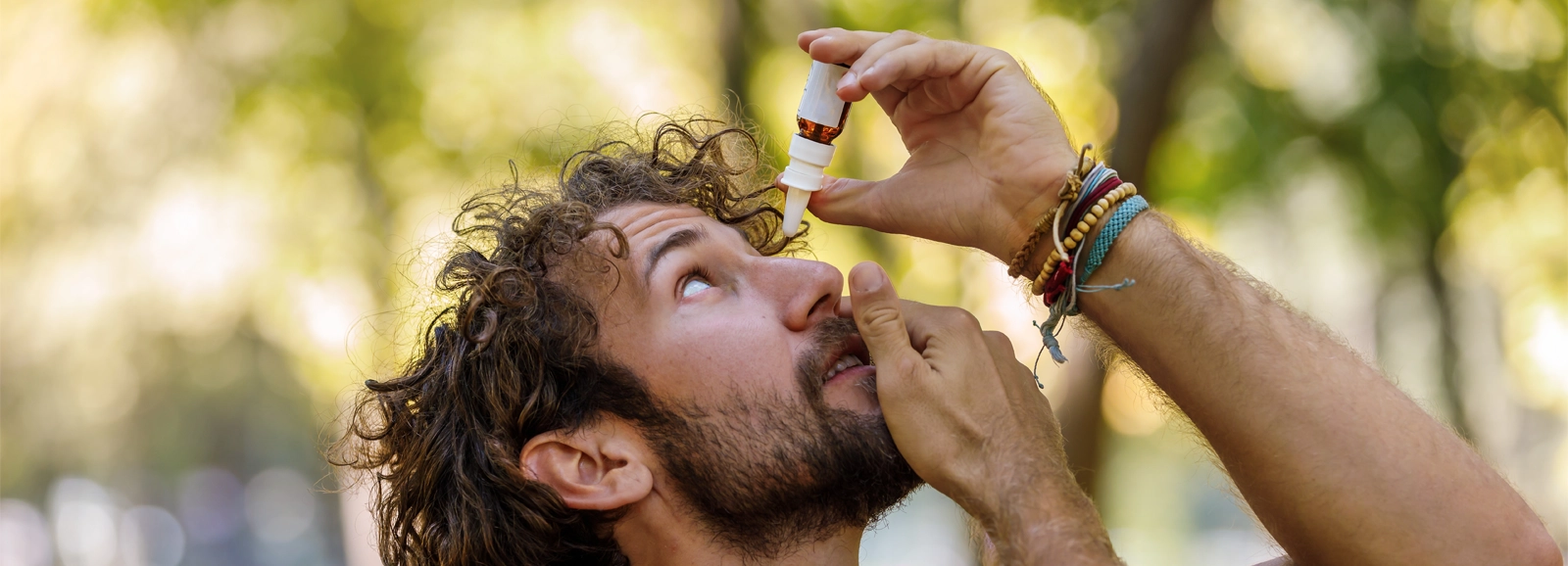 Man outdoors during spring applying eye drops while looking up